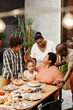 © Seventyfour - Vertical portrait of senior African-American woman celebrating birthday with family and blowing candles on Birthday cake