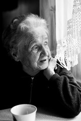 Wall Mural - Portrait of an old lady in her house near the window. Black and white photo.