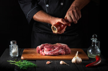 Wall Mural - Professional chef cooking raw meat fillet and adding pepper or chili for marinade on black background. Working environment in kitchen in restaurant or cafe.