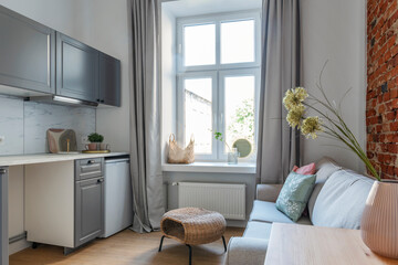 Wall Mural - Cozy room in small apartment with window in hotel. Interior of kitchen with living room in design style. Kitchen furniture and sofa at home.