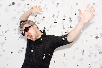 Party fun. Carefree celebration. Holiday entertainment. Festive occasion. Overjoyed happy man in sunglasses dancing enjoying weekend in confetti fall isolated on white background.