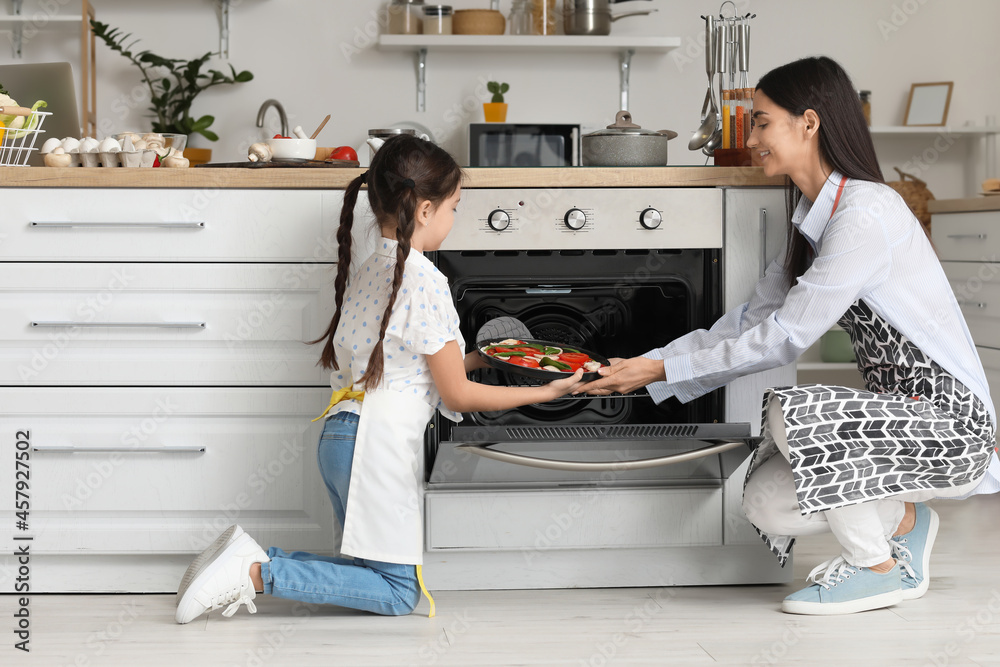 Young mother and daughter cooking pizza in kitchen at home