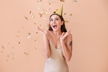 Happy woman in party hat and with flying confetti on color background