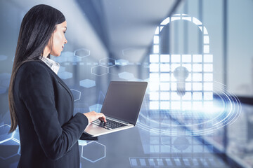 Poster - Attractive young european businesswoman with laptop computer standing in blurry office interior with glowing padlock hologram. Safety and digital security concept. Double exposure.