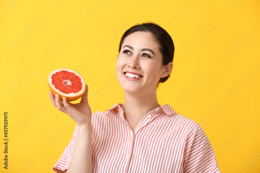 Beautiful young Asian woman with grapefruit on color background