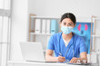 © Pixel-Shot - Female Asian doctor wearing medical mask while sitting at table in clinic