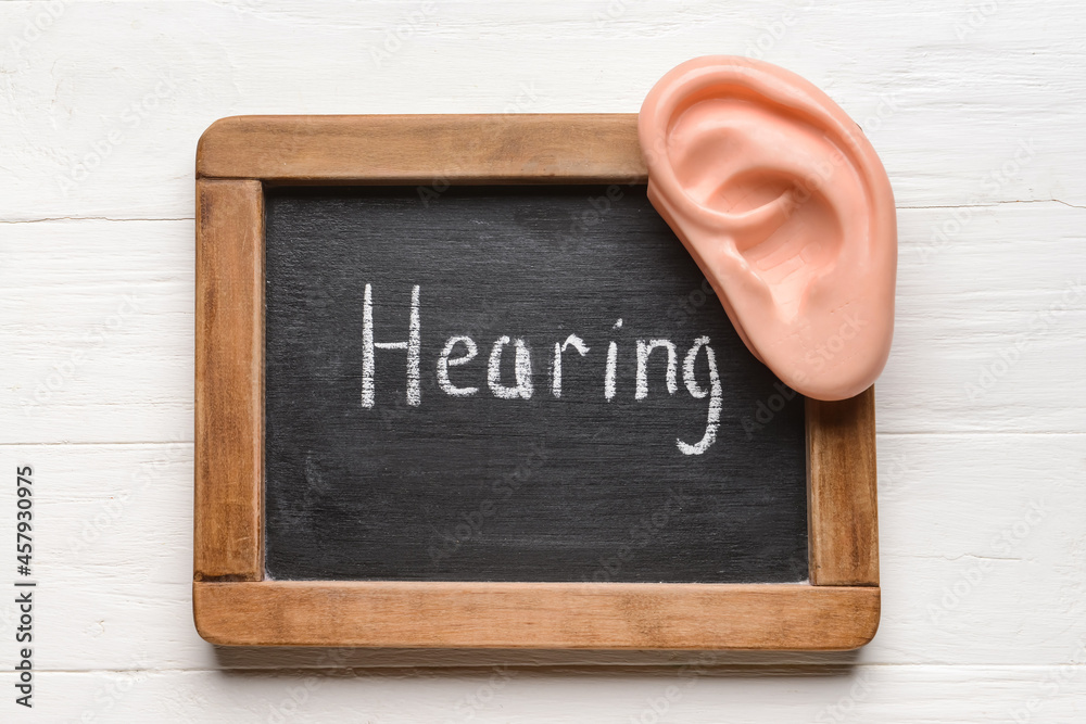 Chalk board with word HEARING and ear model on white wooden background