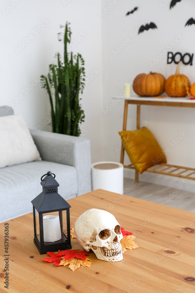 Human skull with candle and fallen leaves on table in room