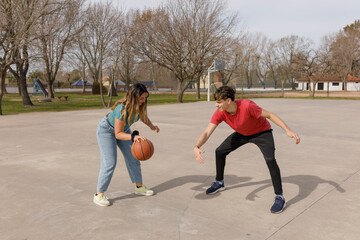  Young couple play basketball in an outdoor public court. Teenagers' hobby. Enjoying free time in a healthy way.