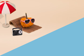 Creative autumn idea with sun umrela and pumpkin hipster in sunglasses laying on the beach.