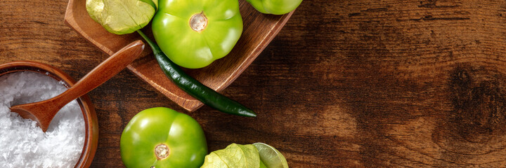 Wall Mural - Tomatillos, green tomatoes, panorama with a place for text. Mexican cuisine ingredients on a dark rustic wooden background, top shot