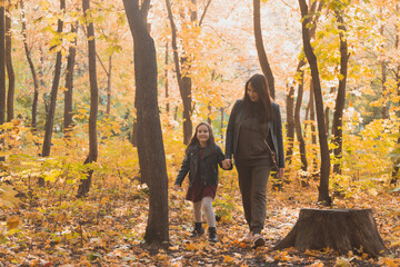 Wall Mural - Young woman and her child girl walking through autumn park. Single parent and motherhood concept.