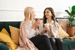 © diignat - Beautiful young woman and adult girl are drinking tea, talking and smiling while sitting on couch at modern home