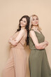 © diignat - Blonde mother and brunette adult daughter wearing identical clothes, different colors, posing over beige background
