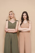 © diignat - Blonde mother and brunette adult daughter wearing identical clothes, different colors, posing over beige background