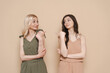 © diignat - Blonde mother and brunette adult daughter wearing identical clothes, different colors, posing over beige background pointing fingers to each other