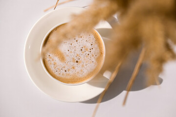 Wall Mural - Pampas grass and white cup with coffee. Drinking Cappuccino in the breakfast morning at home. Flat lay. Wallpaper. Aesthetics