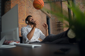 Wall Mural - Cheerful young businessman with headphones and ball taking a break in office, resting.