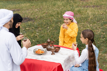 Poster - Happy muslim kids holding tea in glasses near parents in park