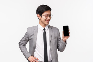 Waist-up portrait of proud professional young asian male office worker, entrepreneur introduce his mobile phone application, showing photos from vacation, show smartphone screen, white background