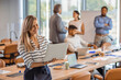© Dragana Gordic - Smiling woman with a laptop in office. Portrait of a smiling confident young businesswoman holding laptop in hand looking at camera with colleague at background in office