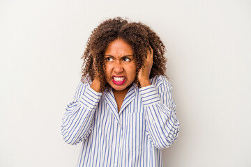 Young african american woman with curly hair isolated on white background covering ears with hands trying not to hear too loud sound.