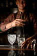 © fesenko - hand of bartender holding long bar spoon and stirring drink in glass with ice