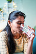 Thirsty young Indian girl drinking glass of pure water during summer - concept of hydration, healthcare.