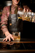 © fesenko - glassy mixing cup from which cold cocktail is poured through strainer into glass on bar counter