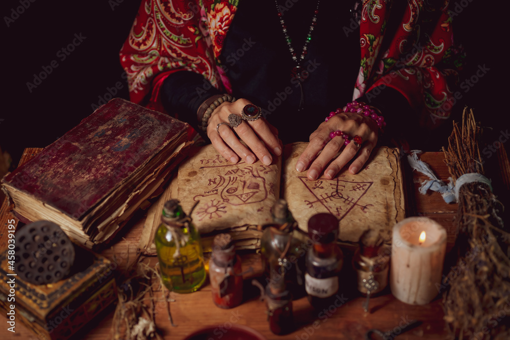 Female witch making potion on dark background, magic bottles with potions and candles on table of alchemist, Halloween theme