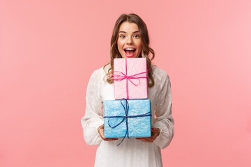 Wall Mural - Holidays, celebration and women concept. Portrait of happy cheerful girl likes celebrating birthday and receive presents, holding two gift boxes and smiling camera, pink background