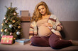 © rubchikova - Beautiful pregnant woman is  sitting on the sofa next to the christmas tree