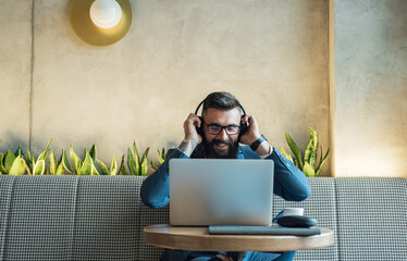 Handsome Businessman Putting Wireless Headphones Before Online Meeting in a Cafe. 
Cheerful smiling business man with headphones having conference call meeting online on laptop computer at restaurant.