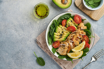 Wall Mural - Fresh green salad with grilled chicken fillet, spinach, tomatoes, avocado, lemon and black sesame seeds, olive oil in white bowl on light slate background. Nutrition Diet Concept. Top view. copy space