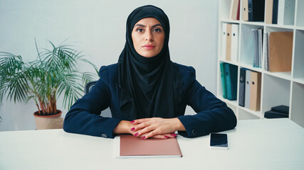 Wall Mural - Muslim businesswoman sitting at desk with smartphone in office