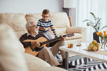 Senior Man Plays Acoustic Guitar To His Grandson At Home.