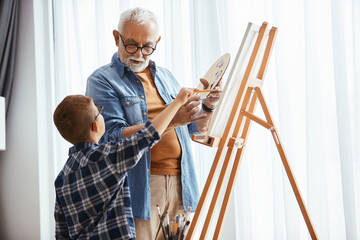 Wall Mural - Grandfather and grandson talk while painting on canvas at home studio.