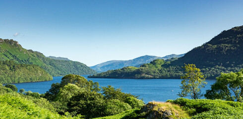 Wall Mural - Along the West highland Way in Scotland. a wide view of the blue waters of Loch Lomond surrounded by green wooded hills on a sunny day