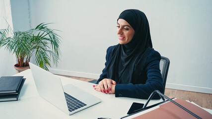 Wall Mural - joyful muslim businesswoman looking at laptop in office