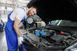 © ViDi Studio - Young technician car mechanic man in blue overalls white t-shirt talk mobile cell on phone stand show troubleshooting process fix problem with raised hood work in vehicle repair shop workshop indoors