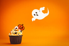 Halloween Cupcake Decored With Jack O'Lantern And Ghost Colored Sprinkles On A Colorful Orange Background