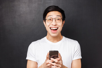 Technology, messaging and people concept. Close-up portrait of excited and amused happy asian man, smiling astonished and pleased, received positive reply in mobile phone messanger, hold mobile