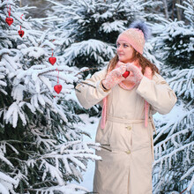 Woman Decorates Christmas Tree With Heart Shaped Balls In Winter Nature On New Year Eve