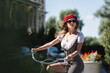 young trendy woman sunglasses, red beret and dress riding bicycle outdoors