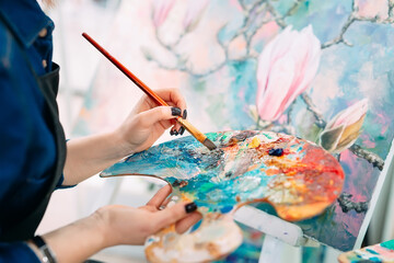 Talented kid holding a professional palette with multi colored paints while working on his new picture in a studio.