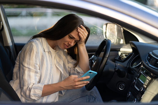 Frustrated girl cry reading sms message in smartphone while driving car. Upset young female break up with boyfriend in traffic jam getting bad news in mobile phone. Unhappy sad woman driver in tears