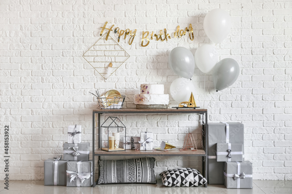 Table with birthday cake and balloons near brick wall