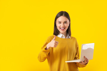 Canvas Print - Beautiful young woman with laptop showing thumb-up on yellow background