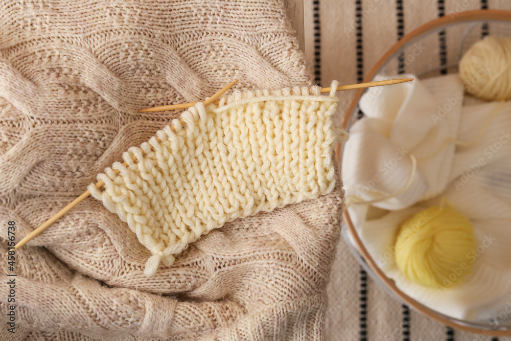 Knitting needles with unfinished clothes on table in room, closeup