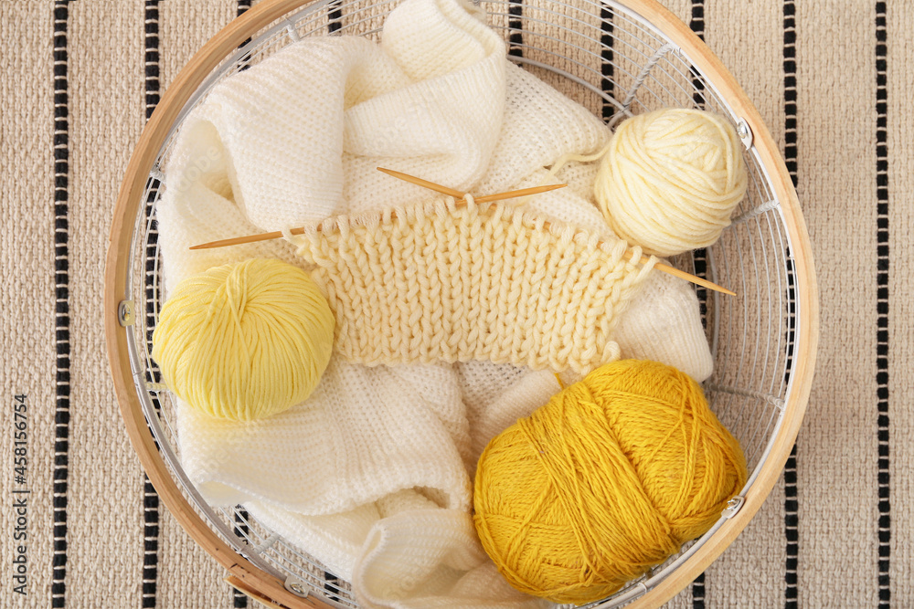 Basket with knitting yarn, needles and clothes on carpet, closeup